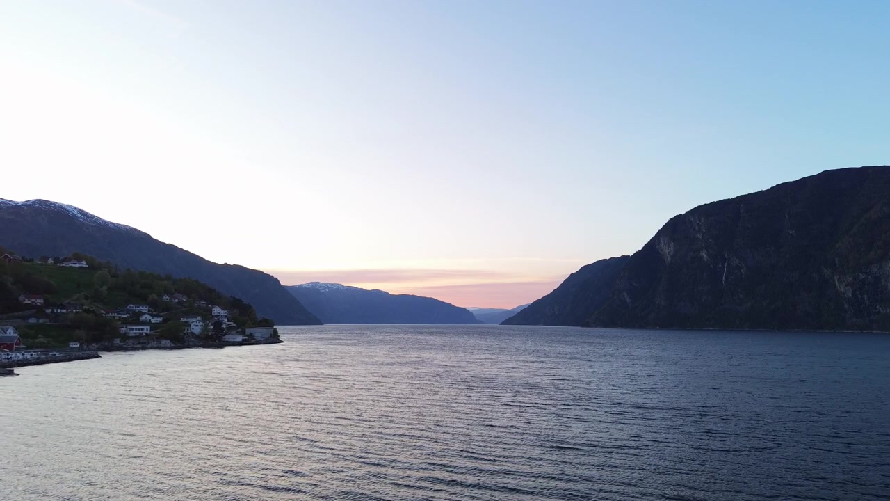 Solen går ned over en stille norsk fjord og kaster et blødt skær over fjerne bjerge. Ideel til rejse- og naturrelaterede projekter.