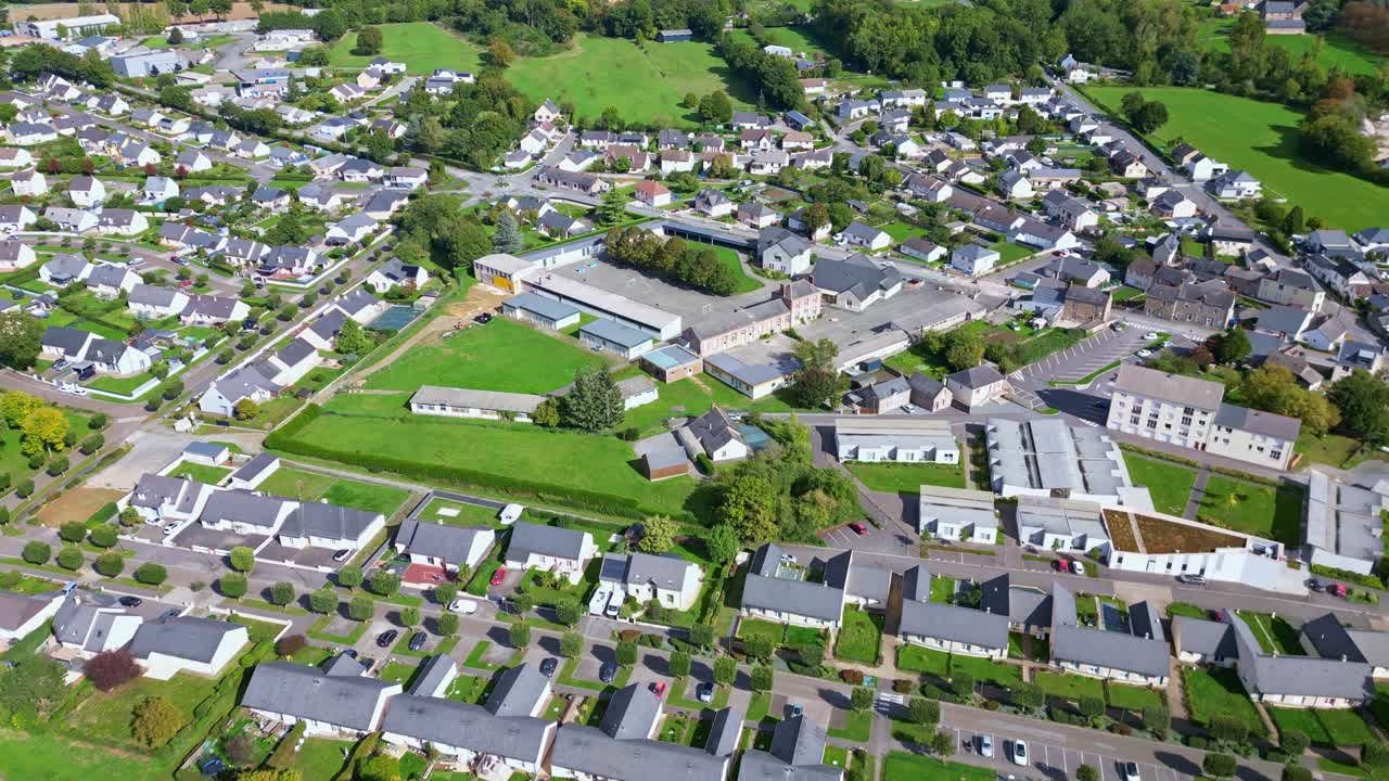 Drone advances above Saint-Pierre-la-Cour, showing residential districts, main road with cars, forest, and fields