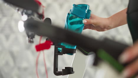 woman puts water bottle in trainer holder in gym closeup. athletic lady prepares refreshing drink for intense jogging training indoors. sportive life