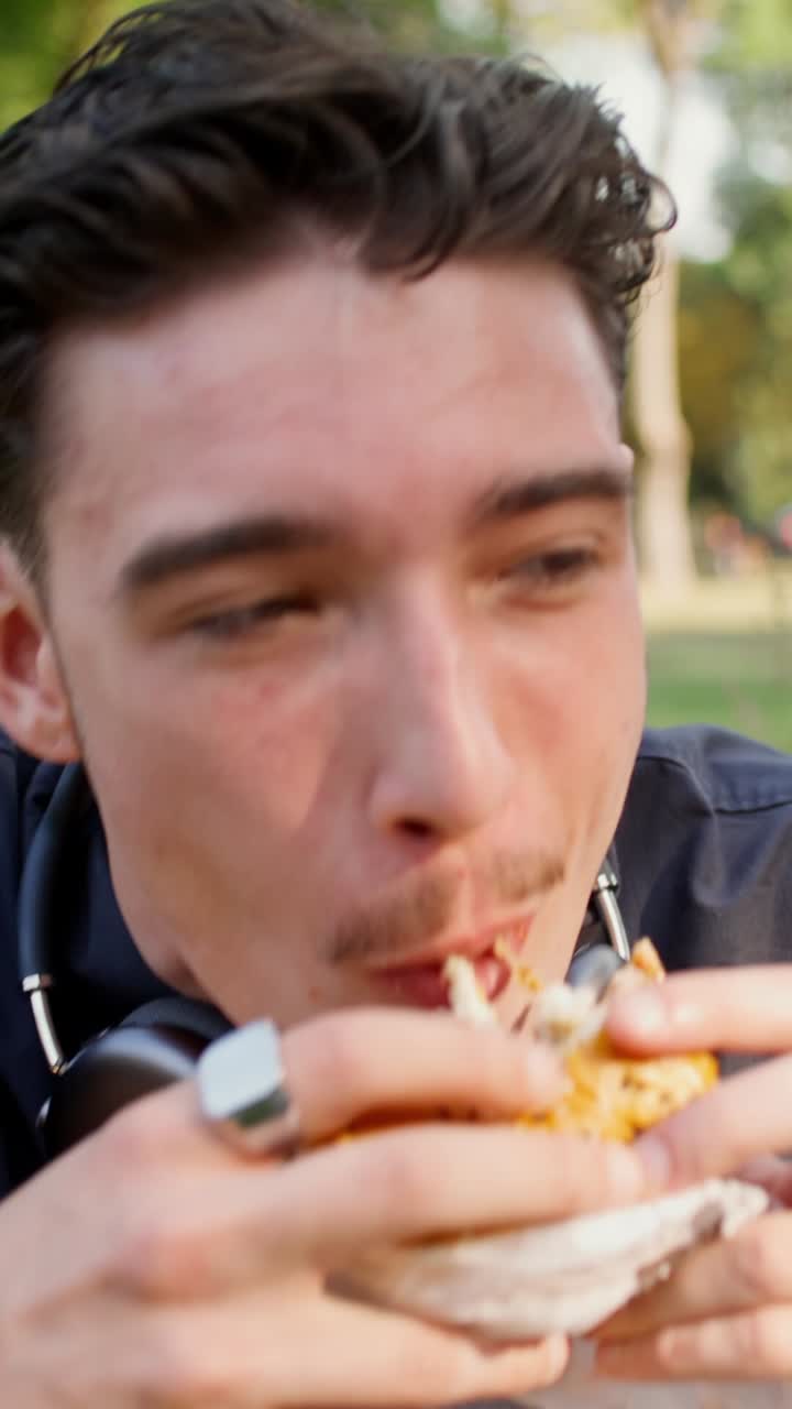 un joven comiendo una hamburguesa en un parque
