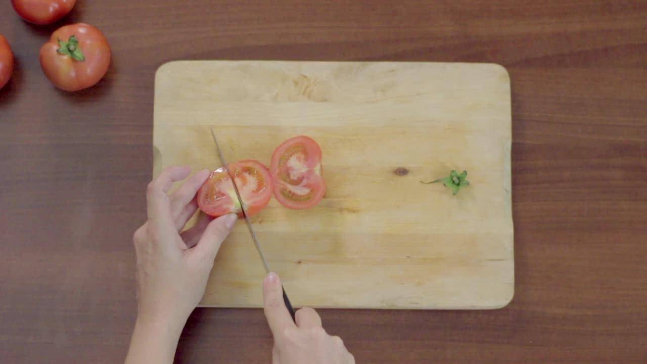 Hände, die eine frische rote Tomate auf einem Holzschneidebrett schneiden