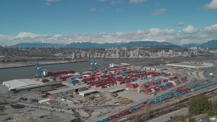 colorful shipping containers stacked high and organized at busy city port harbor dock on edge of fraser river in Surrey BC Canada Aerial wide fixed angle and position