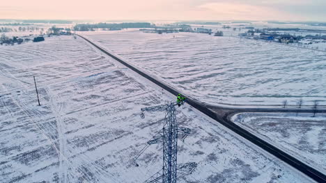 engineer repairing cables atop a tall, metal lattice transmission tower - aerial view