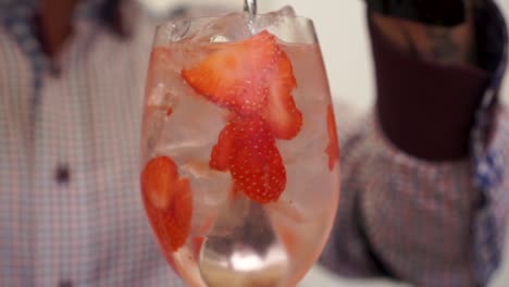 male barman finishing gin and tonic drink coctail with strawberies and ice cubes in glass - close up