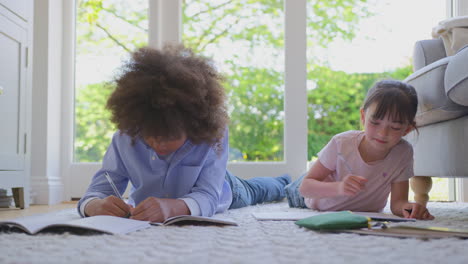 boy and girl lying on rug in lounge at home doing school homework together