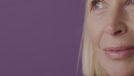 vista de cerca de una mujer madura rubia con ojos verdes sonriendo y mirando la cámara sobre fondo púrpura 1