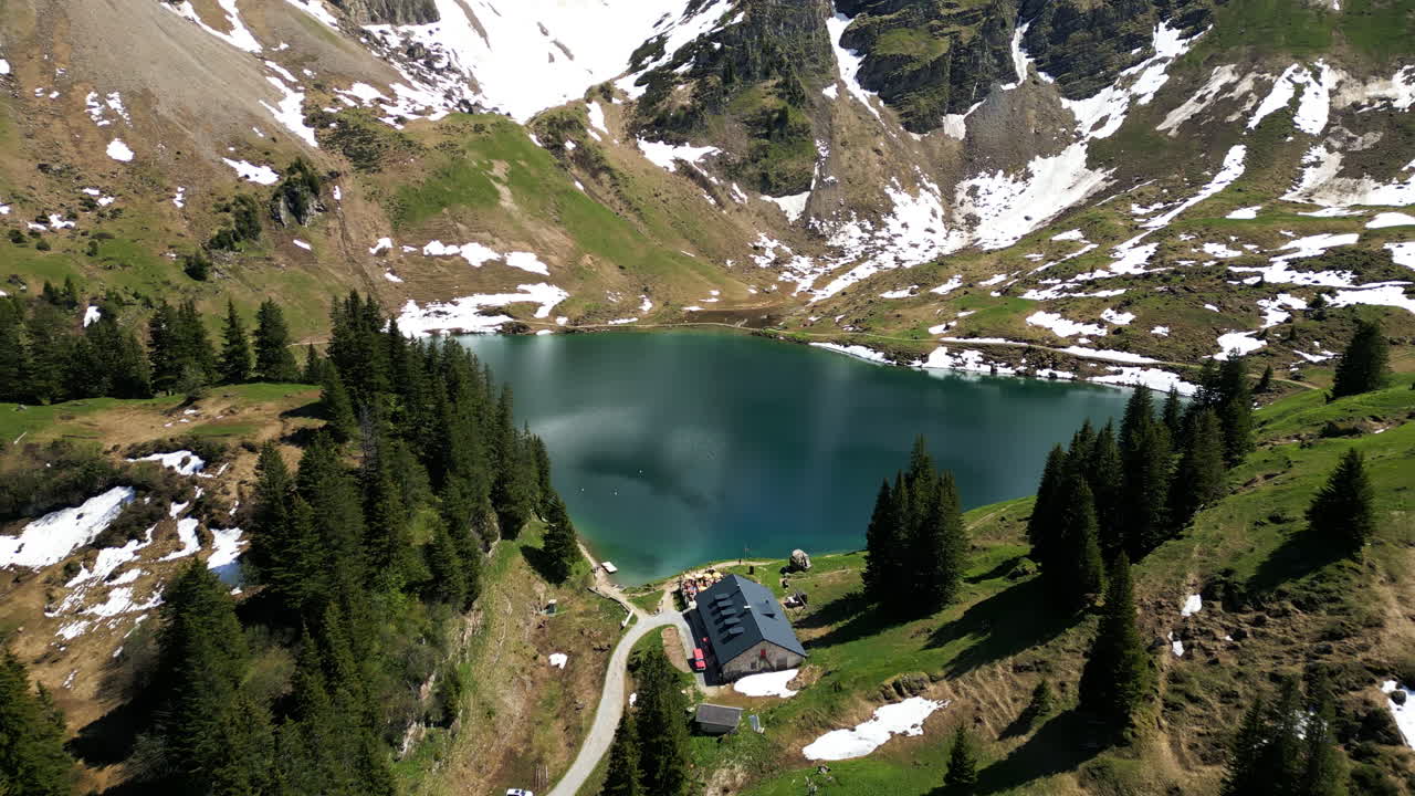 Aerial: Lake Lioson during the day with restaurant and snow in Ormont-Dessous, near Les Mosses, in the canton of Vaud, Switzerland, establishing drone shot