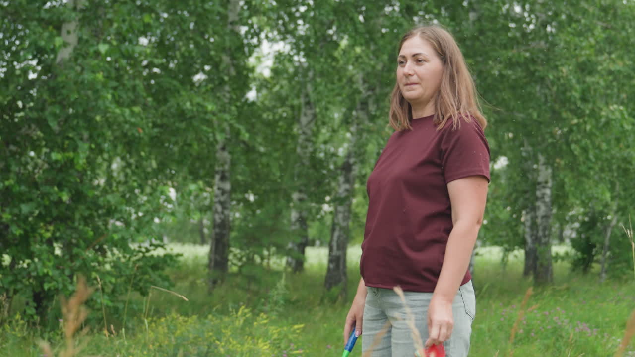 Mujer blanca practicando bádminton en un bosque de abedules; balanceos individuales lentos con raqueta y volante; camisa y vaqueros color burdeos; de pie entre abedules y flores silvestres; los fotogramas muestran a una persona que viaja al trabajo tomándose un descanso