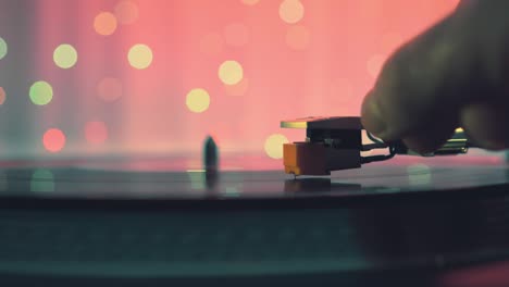 the moment of a rotating vinyl plate turntable on a pink background and bright bokeh lights. sound technology for dj to mix and play music. the man's hand puts and removes needle from the vinyl plate