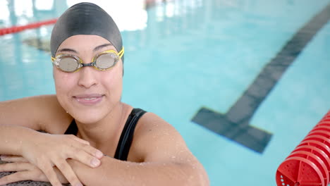 resting at pool edge, female swimmer in goggles and swim cap smiling confidently