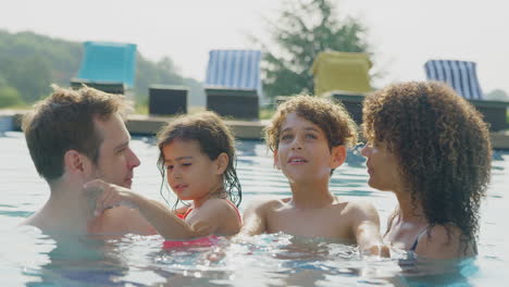 portrait of multi-racial family relaxing in swimming pool on summer vacation together