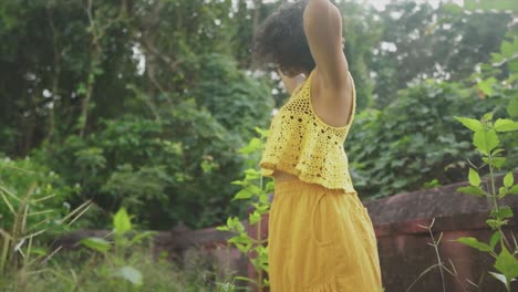 Bonita-Mujer-Morena-Vestida-De-Amarillo-Moviendo-El-Pelo-A-Cámara-Lenta-Sobre-Un-Fondo-Verde-Y-Vegetal