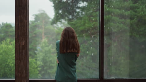 mujer de traje verde mira por la ventana a la lluvia