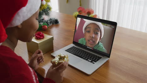 mujer afroamericana con sombrero de santa usando una computadora portátil para una videollamada de navidad con un niño en la pantalla