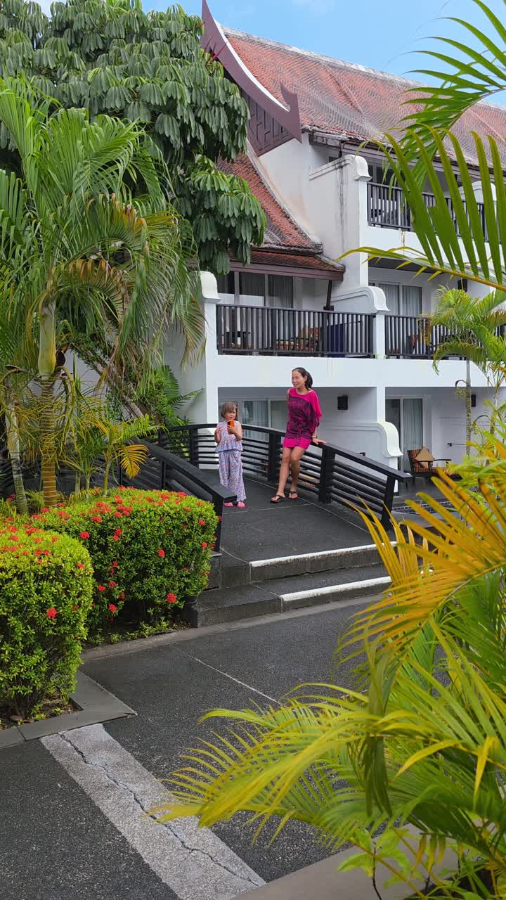 Keluarga menjelajahi lahan subur dan bunga-bunga berwarna-warni di hotel mewah, dikelilingi oleh arsitektur dan tanaman hijau Thailand yang bergaya