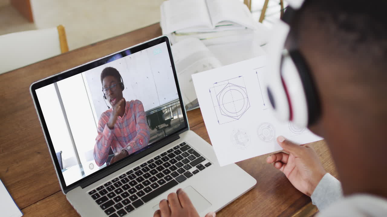 estudiante universitario afroamericano que sostiene notas mientras hace una videollamada en una computadora portátil en casa