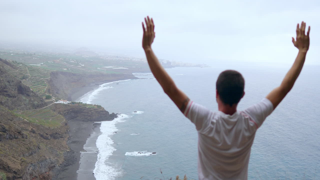 With the ocean before him, a man on a cliff's edge raises his arms and takes in the sea air during a yoga practice, finding serenity
