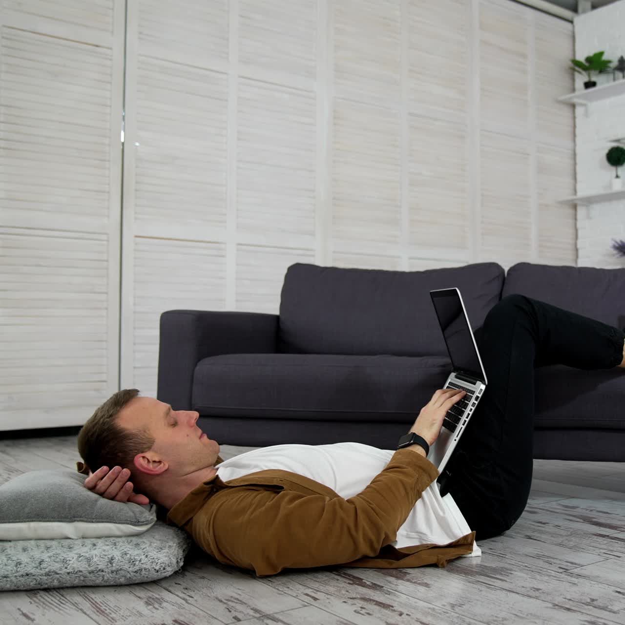 Remote job. Tired freelancer works on a laptop while lying on the floor in the kitchen. Young man studying through the laptop at home. Distance education