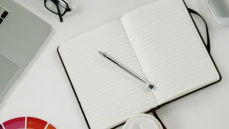 Color-swatch,-laptop,-pen,-organizer,-disposable-glass,-spectacles,-pot-plant-and-pencil-holder-on-w