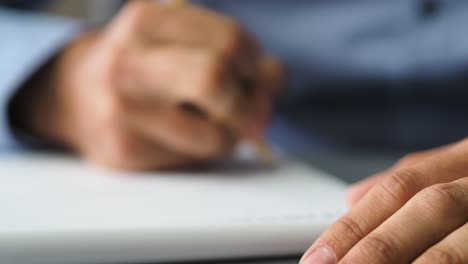 close up shot of man hands noting something in the note book while working in the modern office