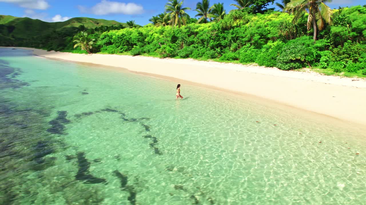 Female in bikini walking from turquoise water onto sandy tropical island beach, Yasawa, Fiji