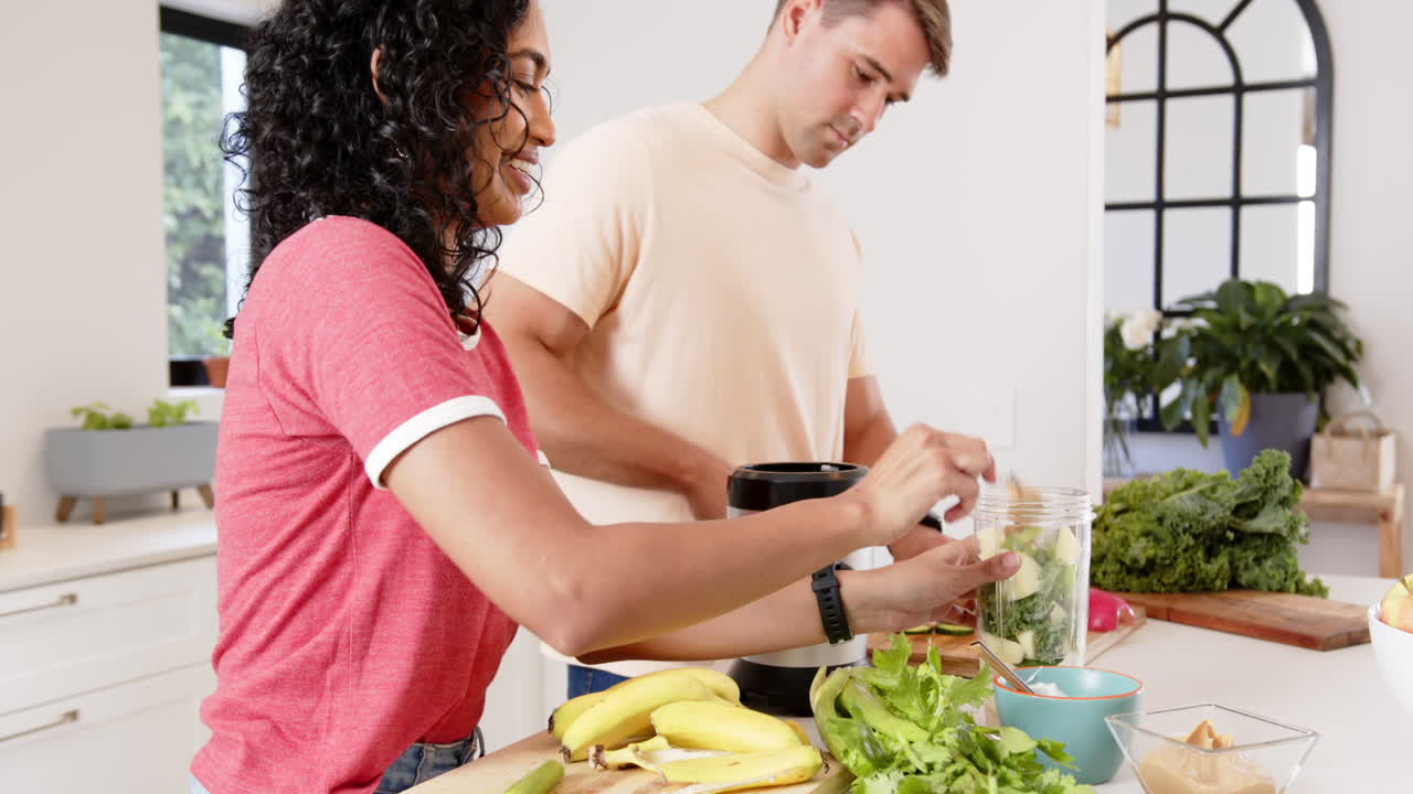 Preparing healthy smoothie, young multiracial couple with fresh fruits and vegetables, at home