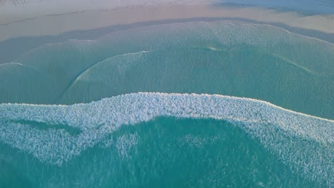 aerial view of turquoise ocean waves crashing on a white sand beach