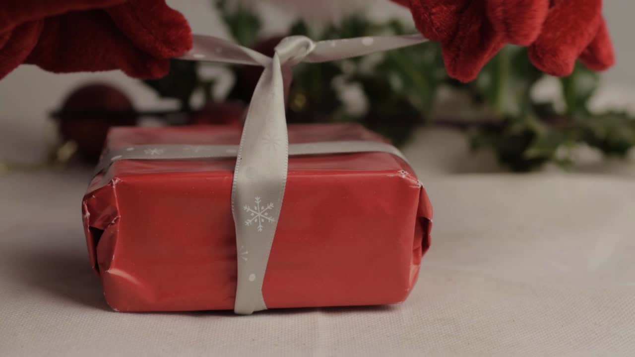 Hand in festive Santa style gloves wrapping a Christmas gift