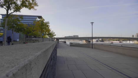 baja rodada hacia delante a lo largo del río en una ciudad moderna con gente caminando y andando en bicicleta, un puente y un paisaje urbano en el fondo, cámara lenta, colonia, alemania