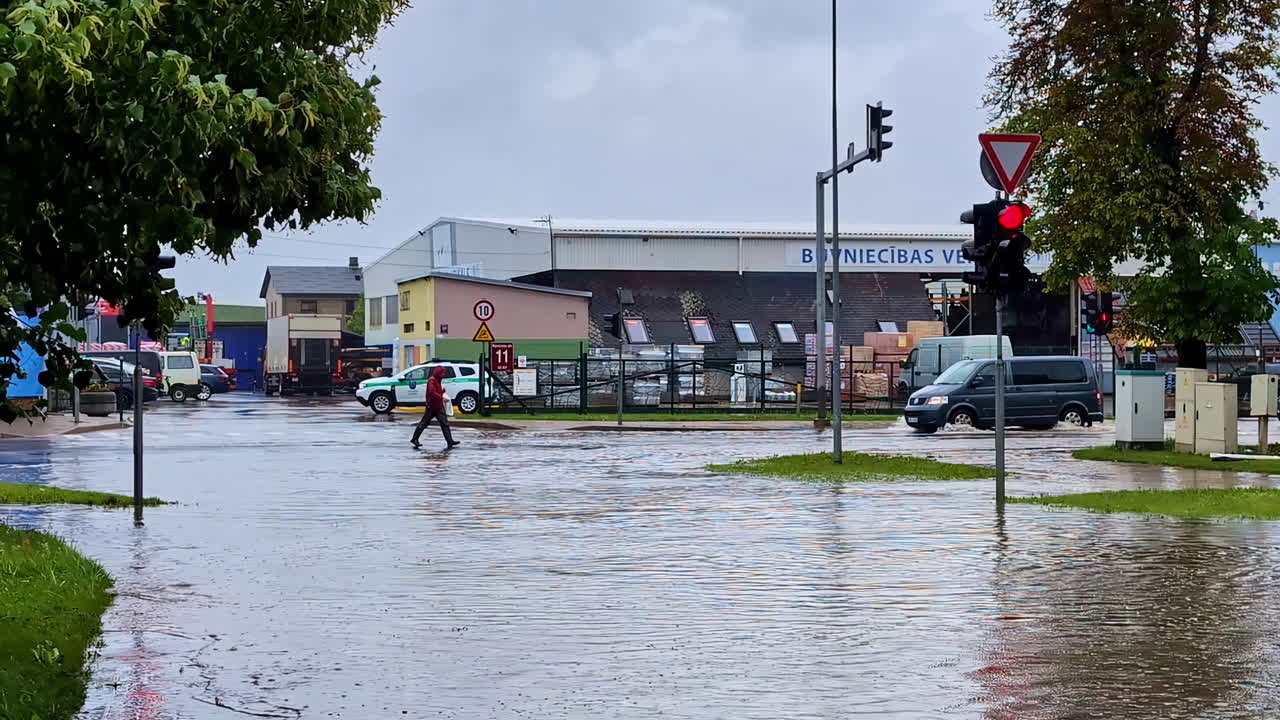 Slow motion landscape of person walking and van vehicle travelling through floodwater crisis disaster risk across street intersection with traffic stop lights weather climate
