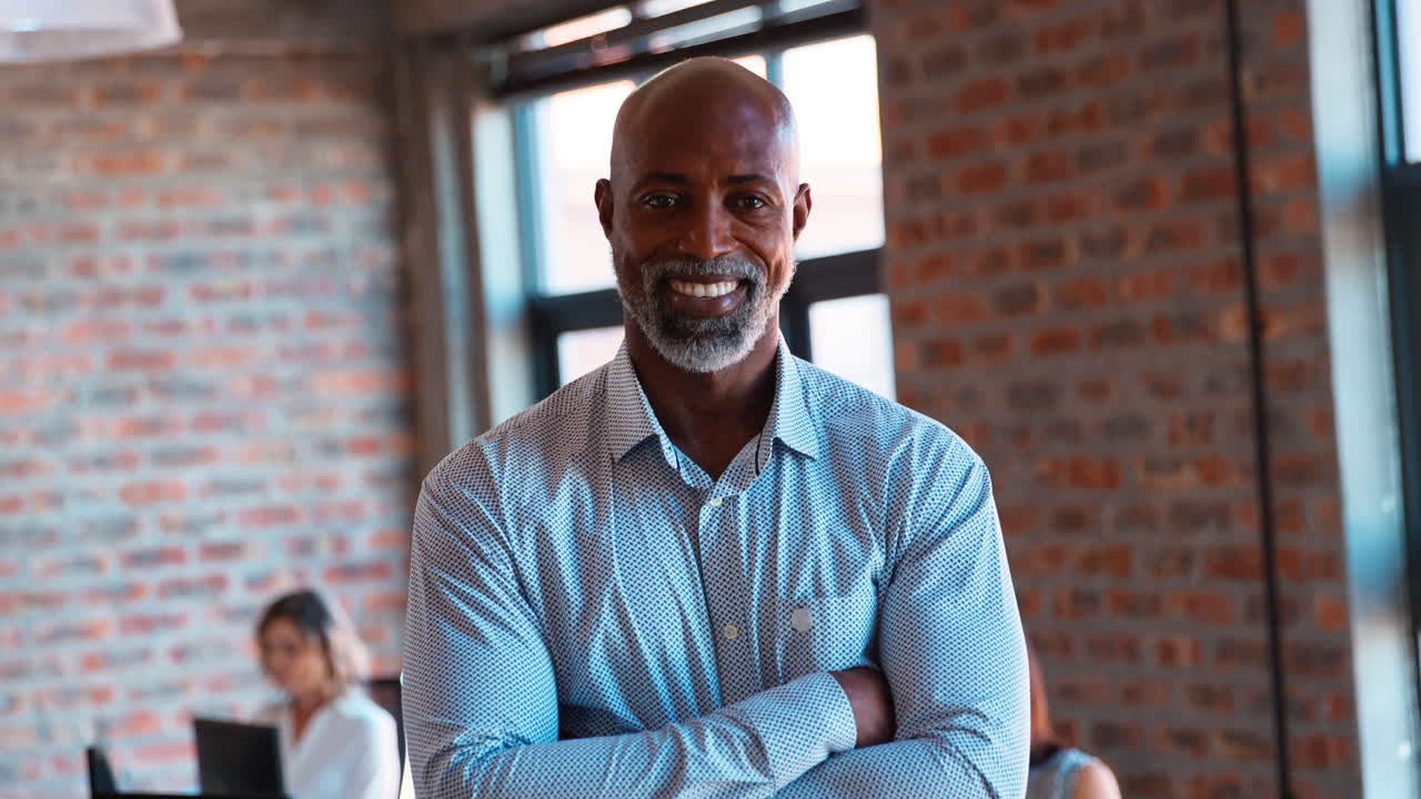retrato de un hombre de negocios maduro sonriente de pie en una oficina ocupada con colegas trabajando en el fondo