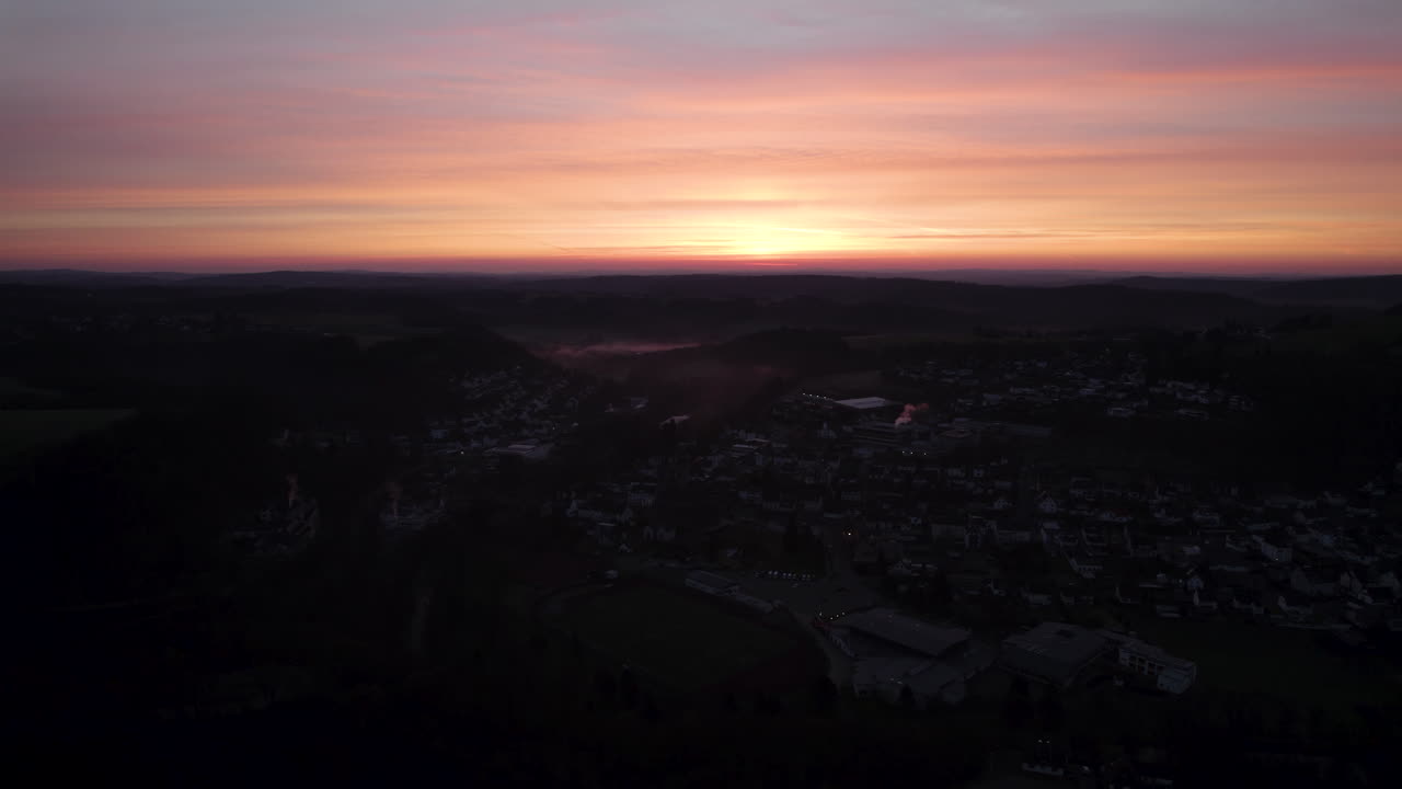 Drone flying over idyllic small town at dawn, capturing a breathtaking vibrant orange-yellow sunrise amidst scenic clouds