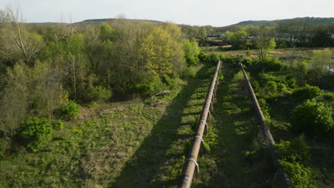 Aerial-shot-of-rusty-pipelines-running-through-a-lush-area-near-Fayetteville,-AR,-in-daylight