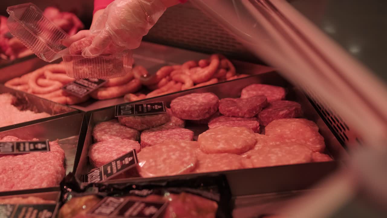 Butcher placing raw meat patties into plastic container at meat counter