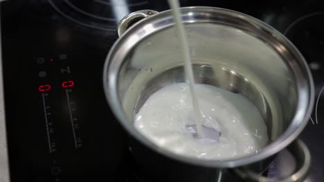 milk being poured into the stainless steel pot for cooking in kitchen