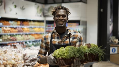 Portrait-Smiling-Worker-At-The-Store-With-Basket-Full-Of-Greens