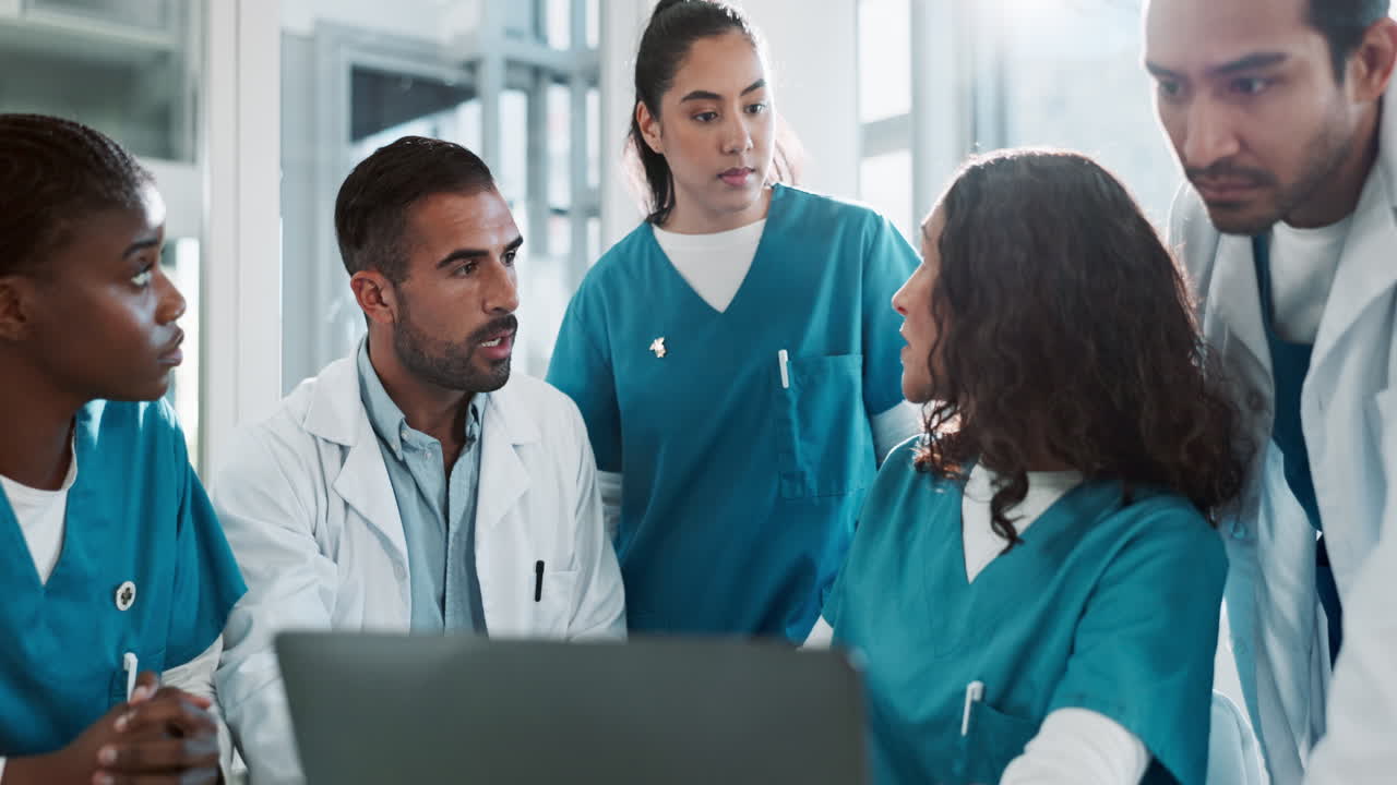 A medical team of doctors and nurses gather around a laptop to discuss patient care.