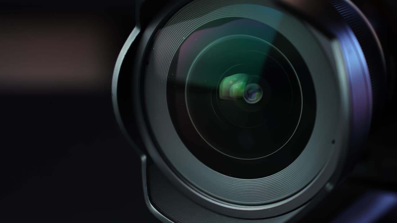 Primo piano a rotazione lenta del vetro frontale di un obiettivo fotografico con riflessi verdi e viola, sfondo scuro da studio e profondità di campo ridotta per b-roll tecnologico di produzione cinematografica.