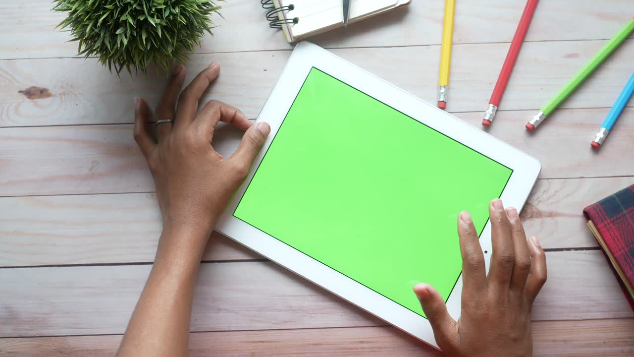Person using a tablet with a green screen on a wooden table