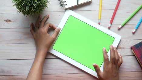 person using a tablet with a green screen on a wooden table