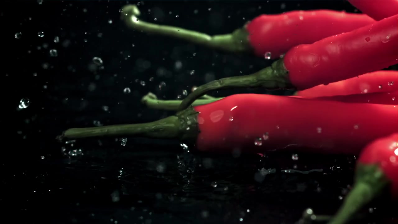 Fresh Red Chili Peppers Splashing into Water in Slow Motion