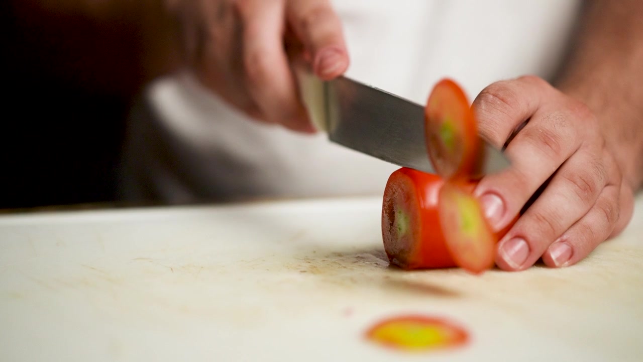 Close-up of a chef slicing a juicy Italian tomato with a sharp knife on a rustic cutting board