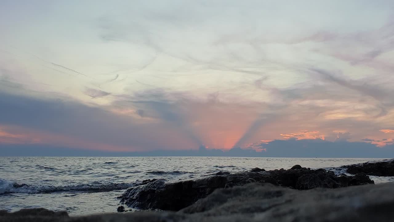 Low angle shot of a rocky coast with waves crashing during a vibrant sunset
