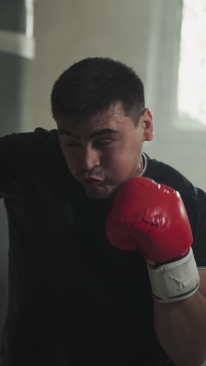 un boxeador golpea una bolsa de peluche bloqueando la cara en un club deportivo. un deportista entrenado golpea el equipo en un gimnasio de boxeo en cámara lenta. técnicas de combate rendimiento