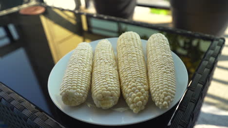 placing freshly husked sweet corn on a glass plate