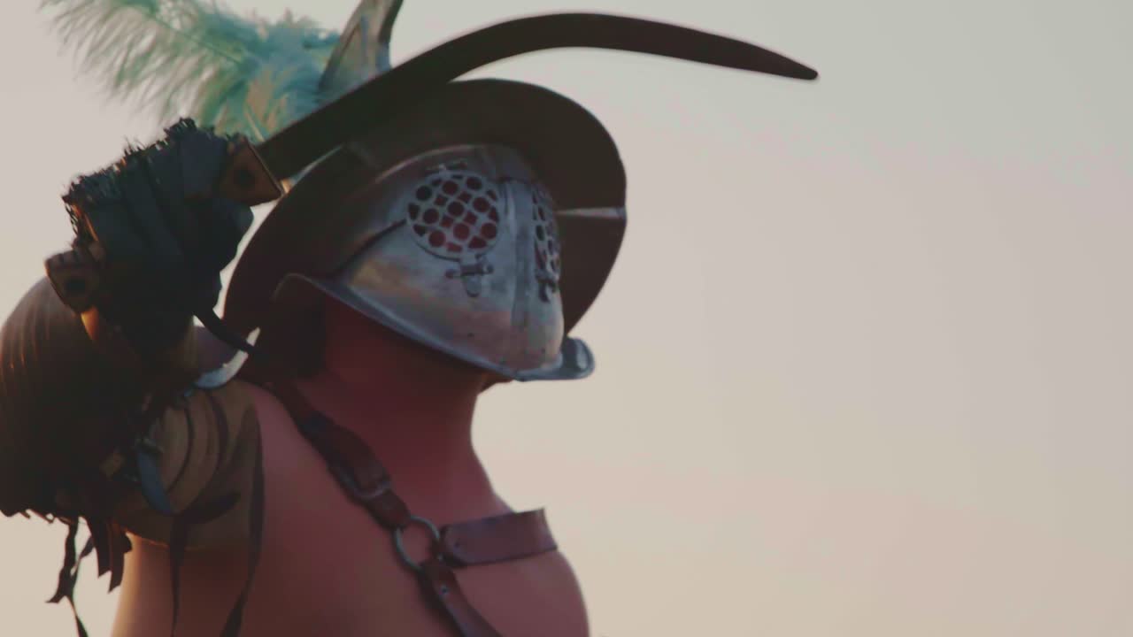 A cinematic, dramatic close-up of a Roman gladiator in detailed armor and crested helmet (galea), slowly raising a curved sword (sica) with a focused, intense action shot against a hazy sky