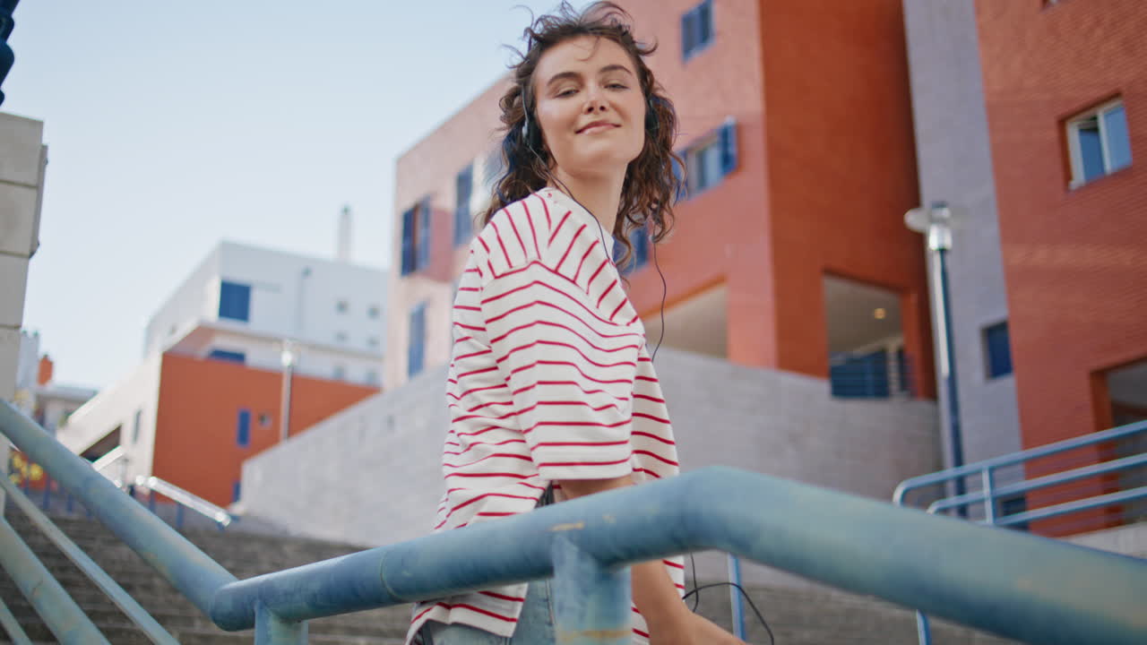 una chica retro disfruta de la música con auriculares apoyándose en las barandillas urbanas de cerca.