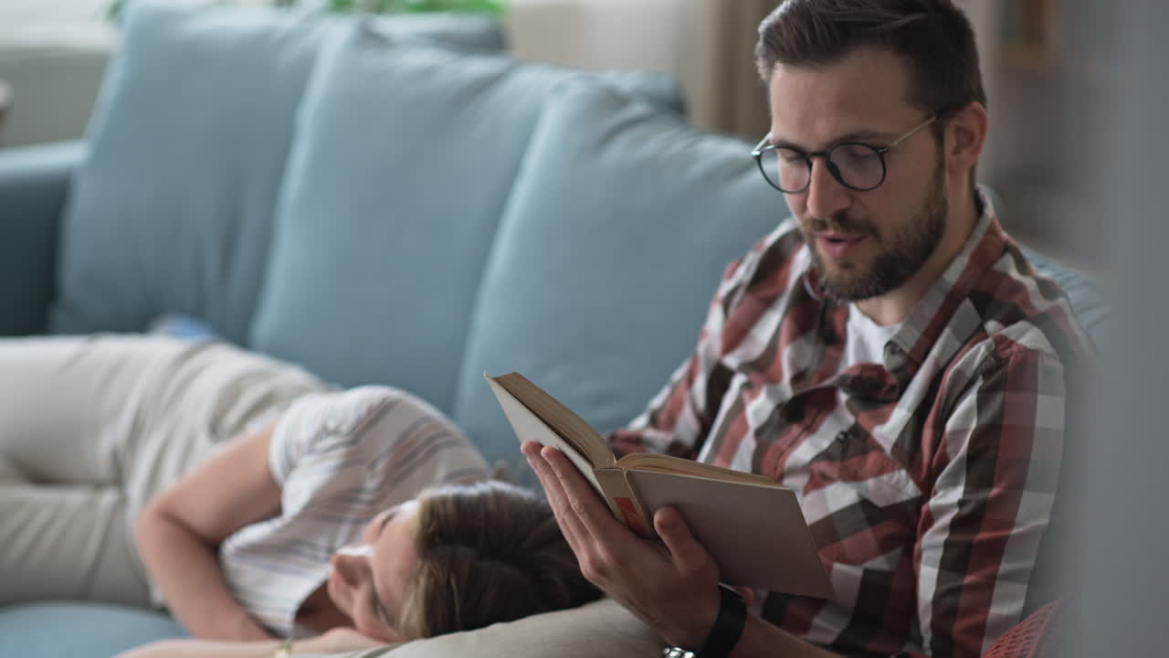 Couple Relaxing at Home with Man Reading a Book