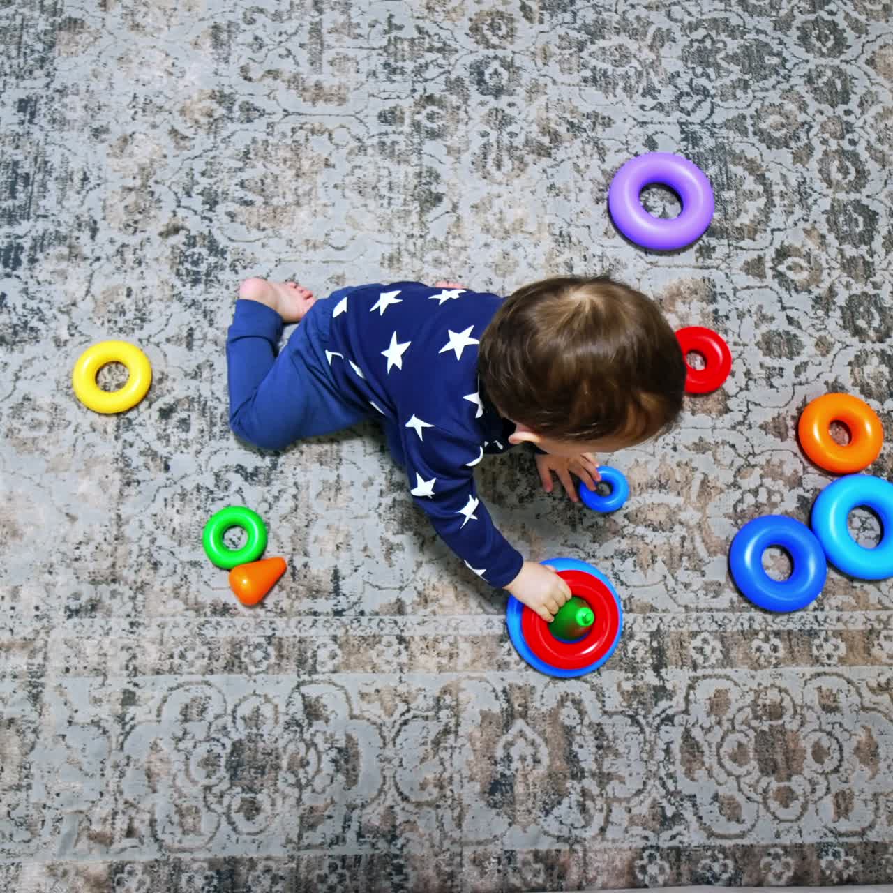 Bambino che raccoglie gli anelli colorati della piramide. Bambino moro seduto sul pavimento che gioca con un giocattolo. Vista dall'alto