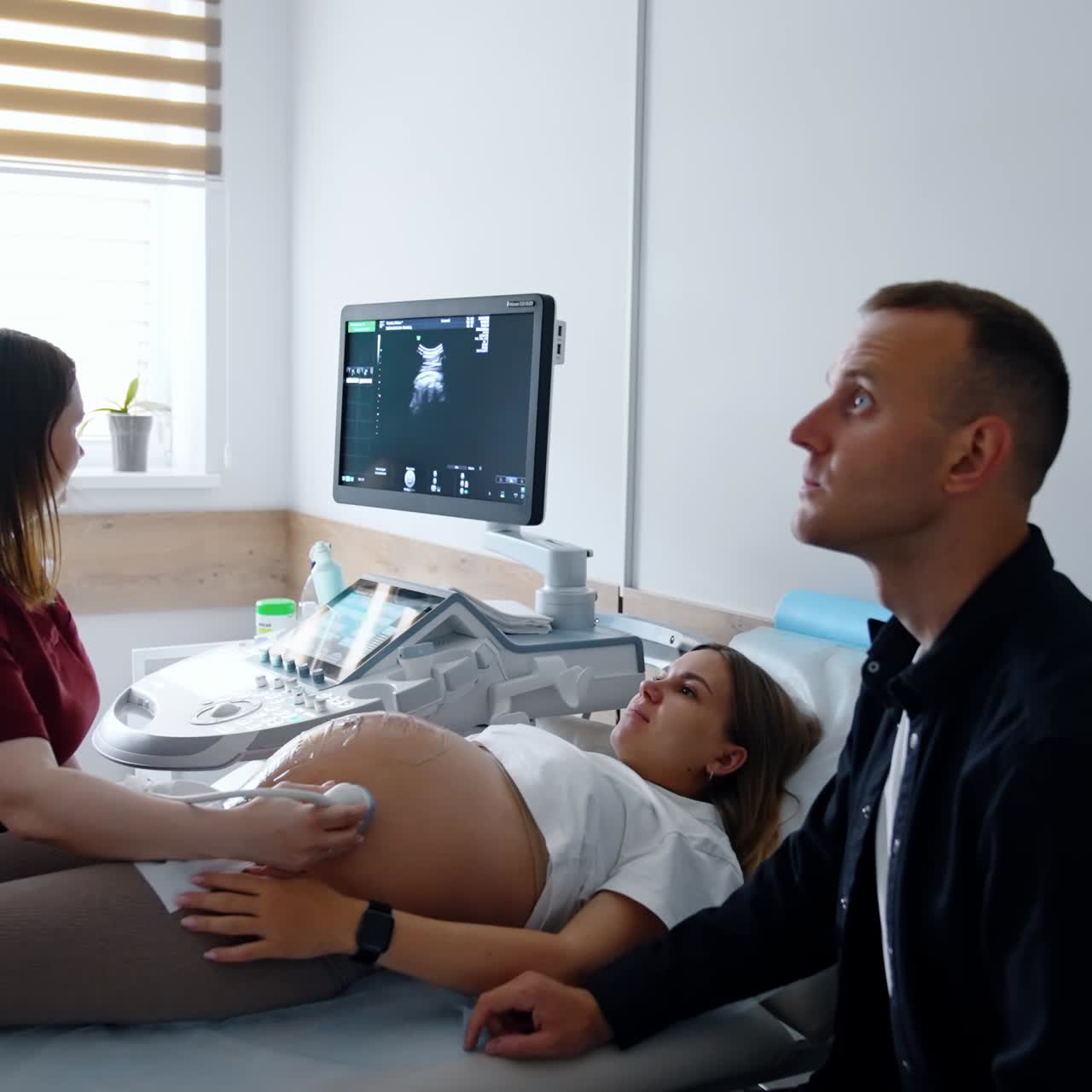Female doctor performs ultrasonic check for pregnant woman. Expecting parents look attentively on the monitor